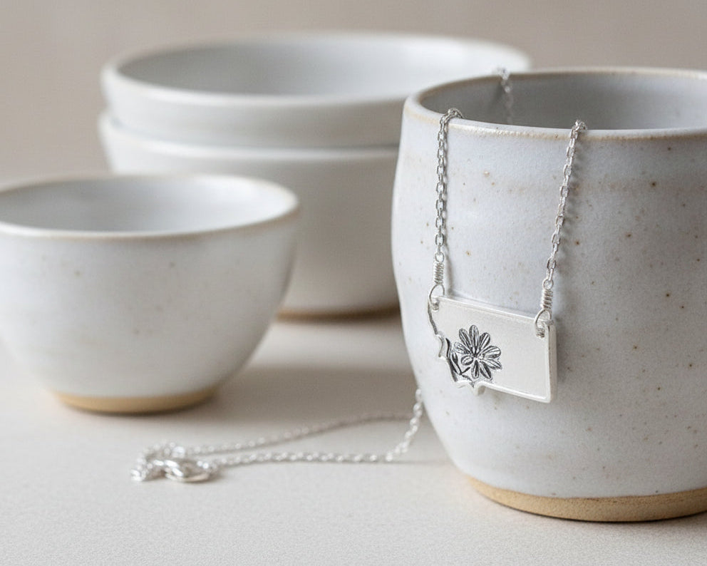 Ceramic bowls with a necklace featuring a silver tag on a neutral background